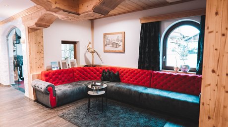 Einblicke in unser Hotel im Stubaital in Fulpmes Gemütliche Sofaecke mit rotem und grauem Samt und Holzbalken