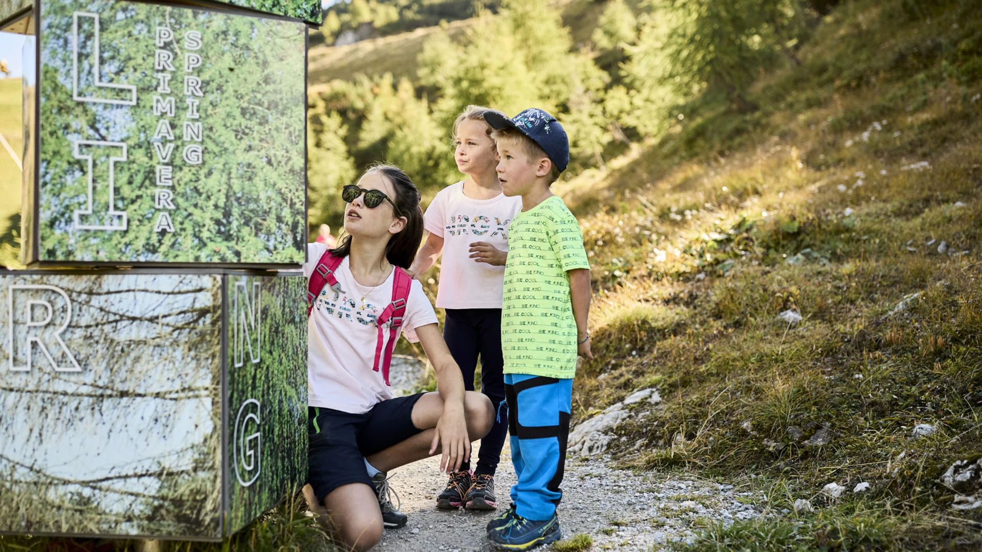 Woman and two children stand on a mountain trail beside a large sign
