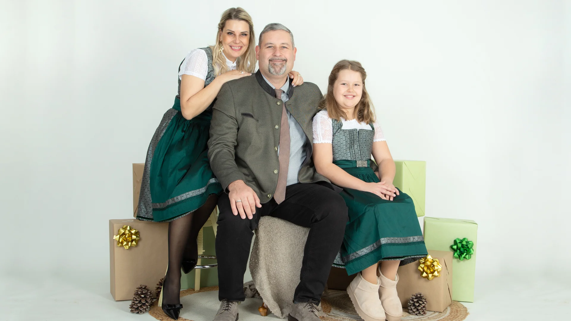 Three people in traditional clothing surrounded by gift packages and pine cones