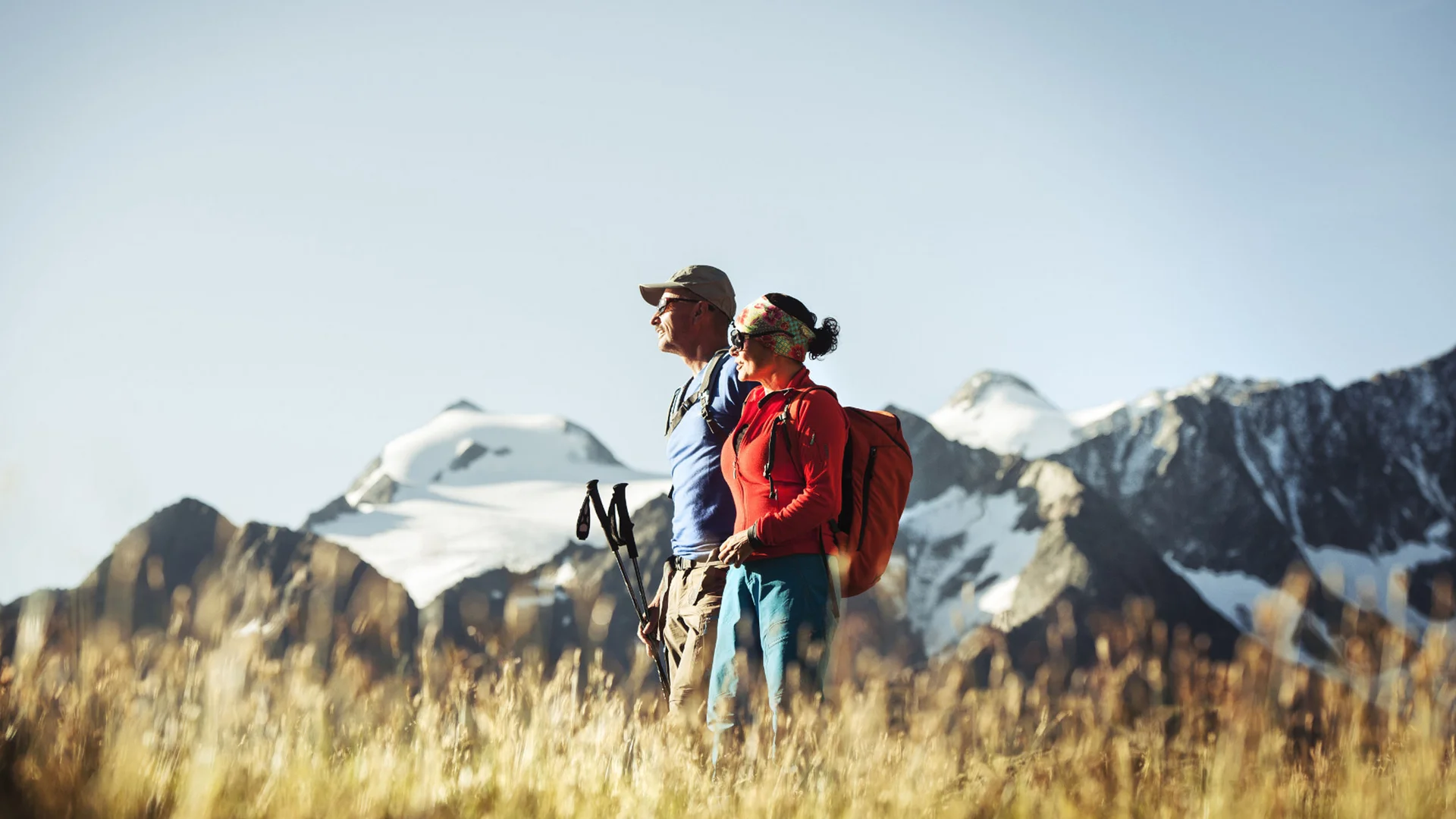 Two hikers with backpacks against a snowy mountain landscape