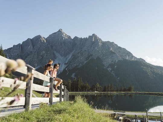 Sommerurlaub im Stubaital: nicht ohne meine Stubai Super Card Familie genießt Bergblick an einem ruhigen See mit Holzzaun im Vordergrund