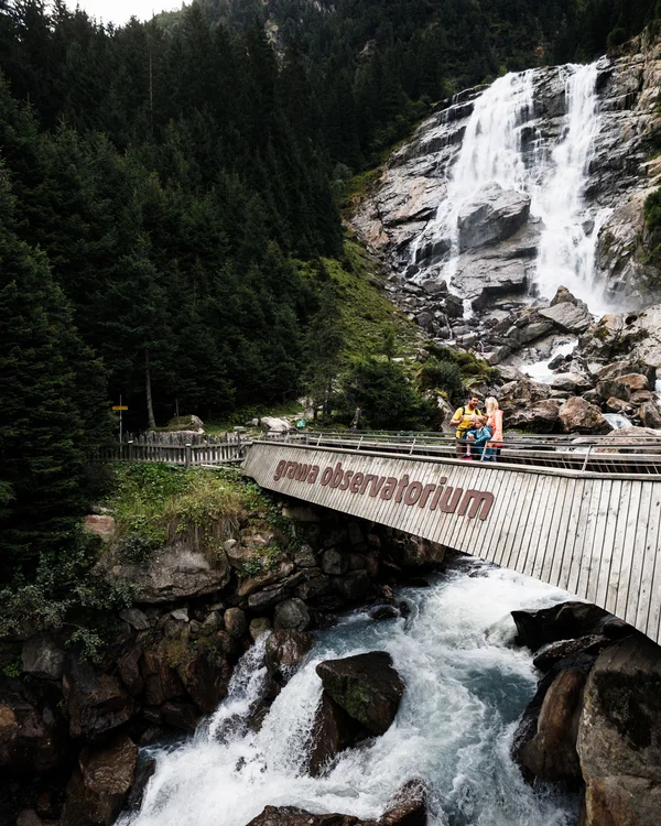 Hotel Alphof | your basecamp for walking holidays in Austria Wooden bridge at Grawa Waterfall with visitors in a dense conifer forest