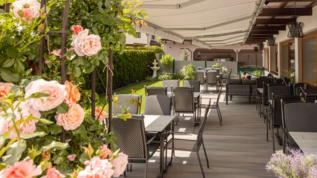 Einblicke in unser Hotel im Stubaital in Fulpmes Überdachte Terrasse mit Tischen und Stühlen neben blühenden Rosen im Garten