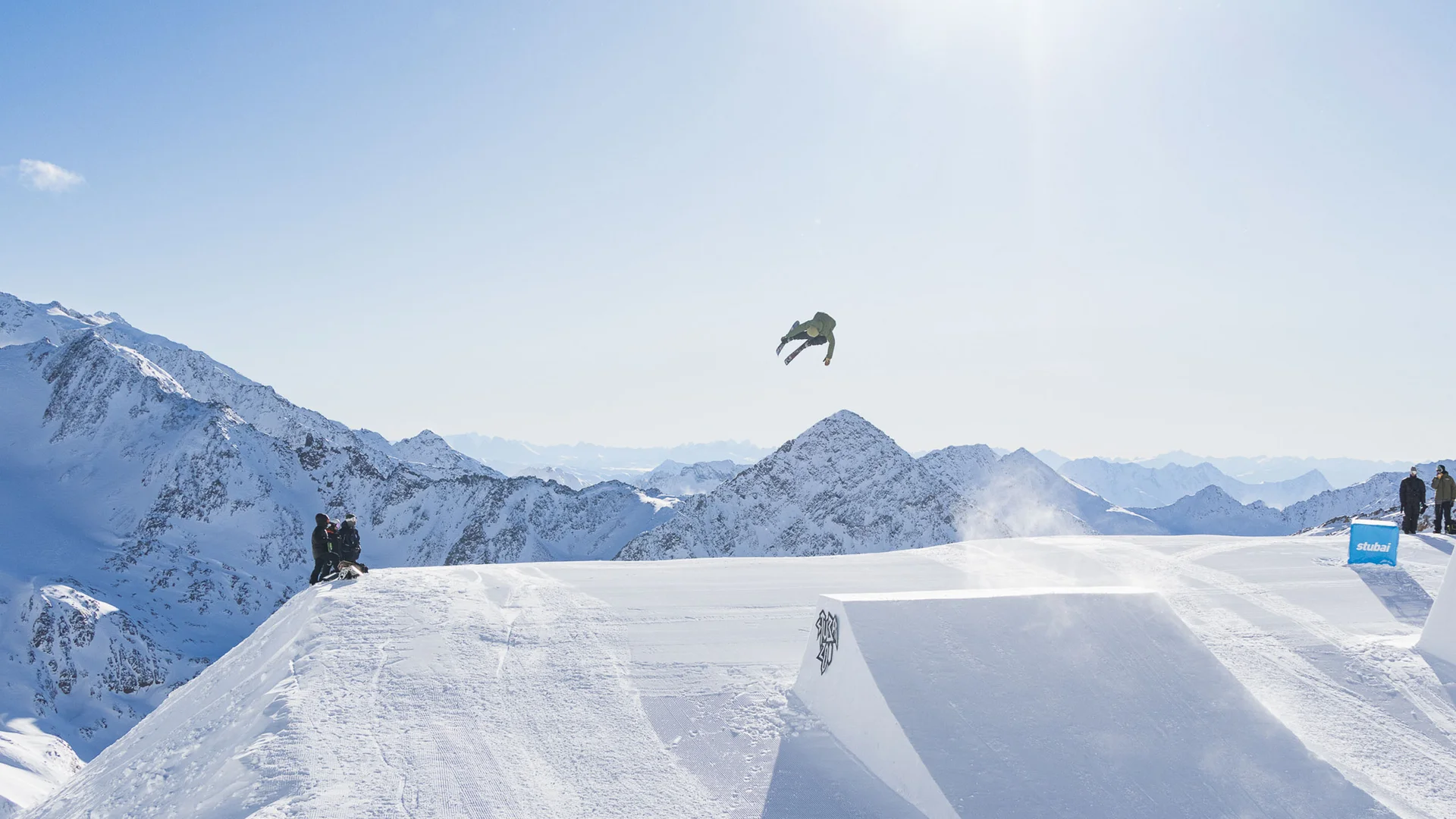 Skier jumping over a snowy ramp with a mountain panorama