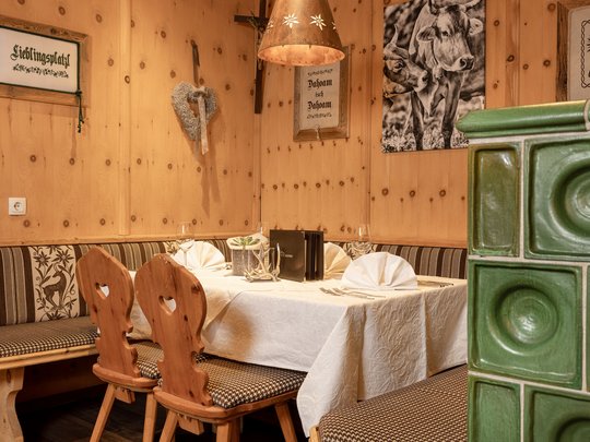 My hotel in Fulpmes in Stubaital Cozy wooden room with table, bench, two wooden chairs, and green tiled stove