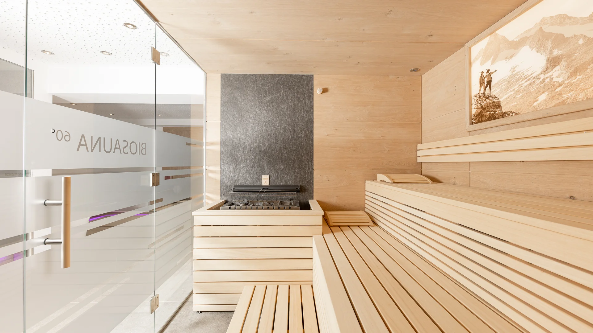 Bright wood sauna with benches, glass wall and mountain picture