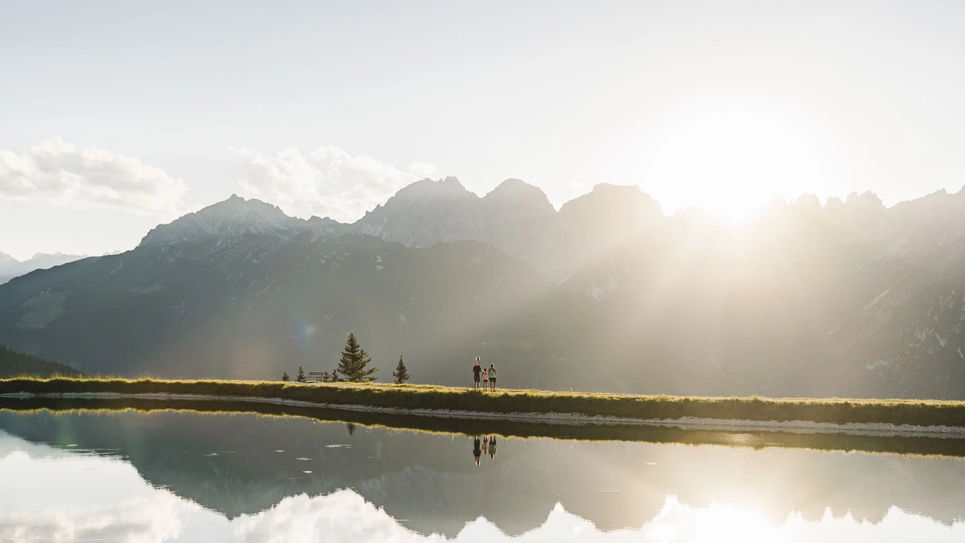 Mountain panorama with three hikers by a lake in sunlight