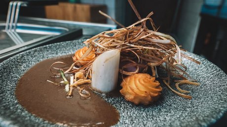 Einblicke in unser Hotel im Stubaital in Fulpmes Kreatives Gericht mit Sauce, Chipspüree und frittierten Gemüsestreifen auf grauem Teller