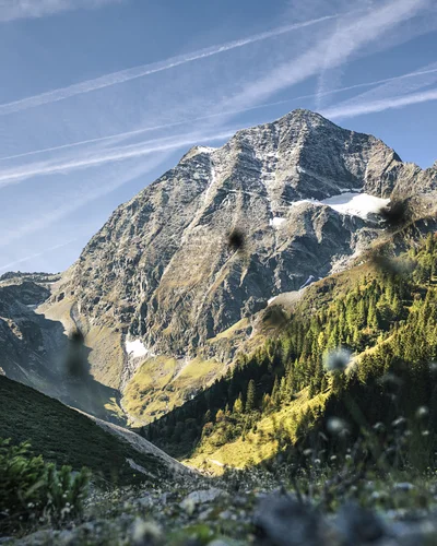Hotel Alphof | your basecamp for walking holidays in Austria Mountain landscape with a snow-dusted peak, rocky cliffs and forested slopes