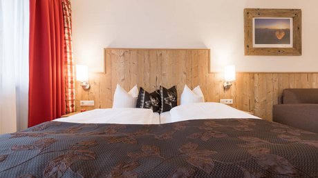 Einblicke in unser Hotel im Stubaital in Fulpmes Gemütliches Doppelbett mit Holzkopfhaupt und brauner Tagesdecke in einem hellen Zimmer