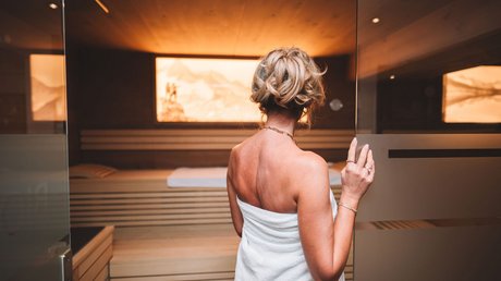 Einblicke in unser Hotel im Stubaital in Fulpmes Frau mit Handtuch betritt eine Sauna mit warmer Beleuchtung