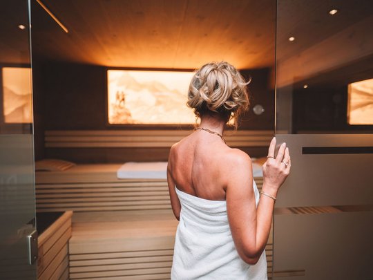 Unser Wellnesshotel im Stubaital Frau mit Handtuch betritt eine Sauna mit warmer Beleuchtung