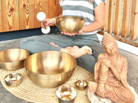 Unser Wellnesshotel im Stubaital Frau meditiert mit Klangschalen und einer Buddha-Statue auf einem Teppich vor Holzwand