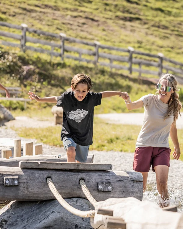 Alphof in Fulpmes, Tyrol | Attractions Mother and boy cross a wooden footbridge over a mountain stream