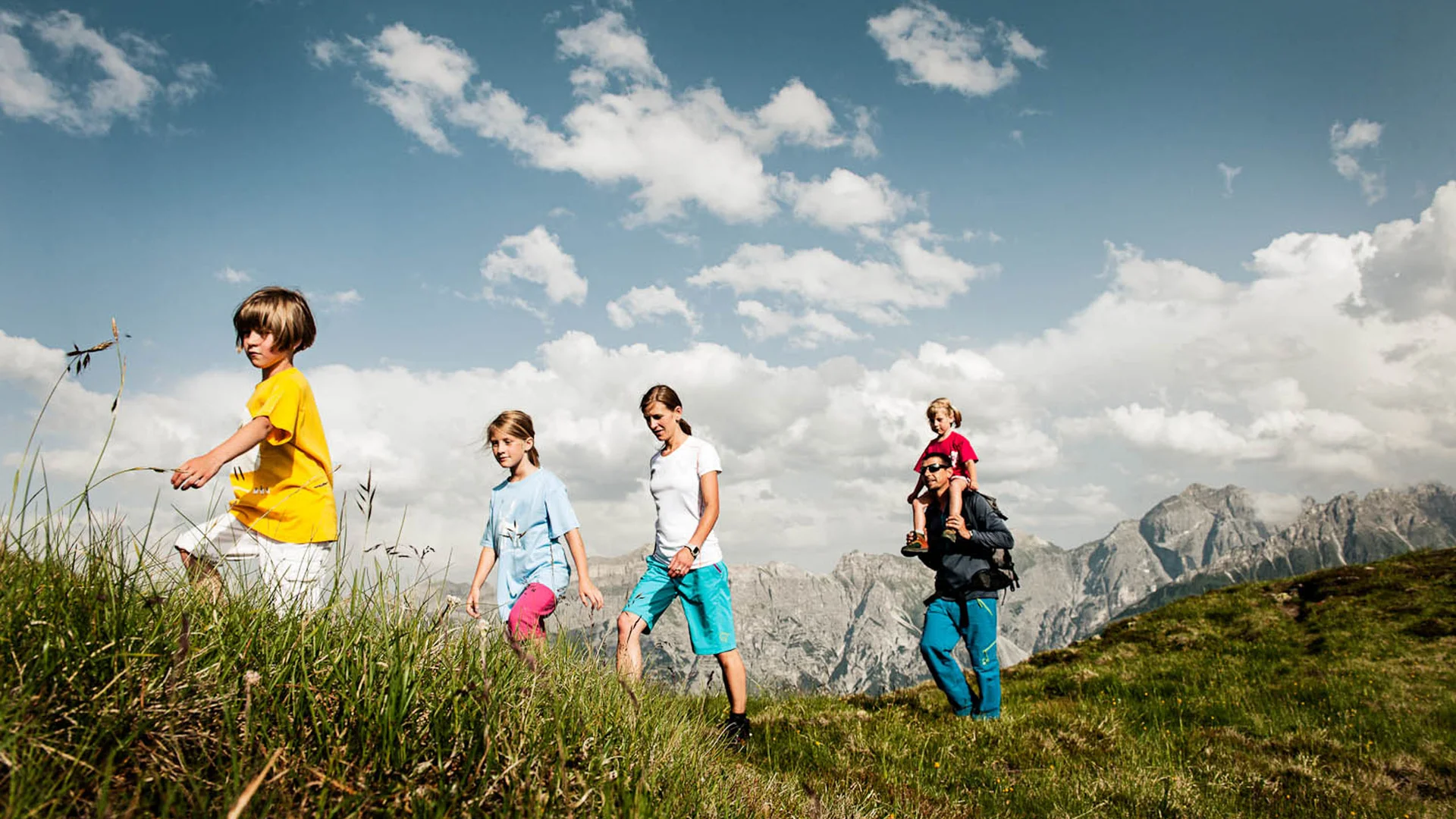 Family hiking across an alpine meadow with dramatic mountains in the background