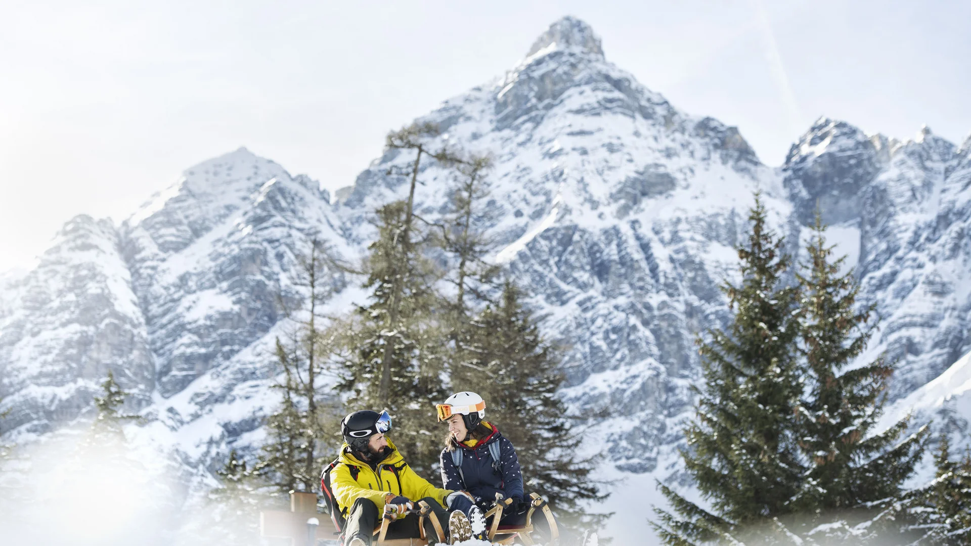 Two skiers in the snow before snow-covered peaks and fir trees