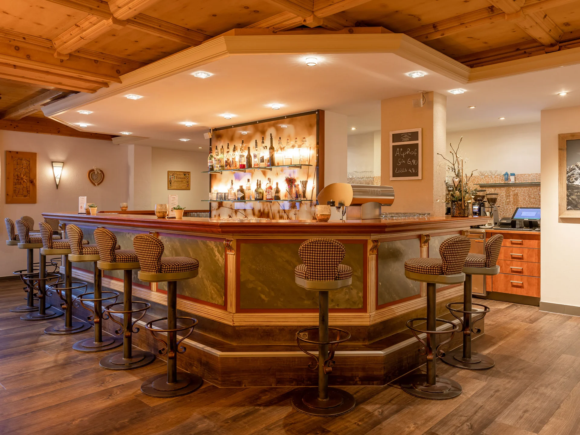 Alphof | genuine indulgence at a gourmet hotel in Tyrol Rustic hotel bar with wooden ceiling, bottle shelves and upholstered bar stools