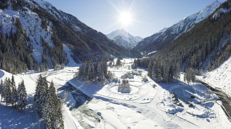 Einblicke in unser Hotel im Stubaital in Fulpmes Sonnige Winterlandschaft mit schneebedeckten Bergen und gefrorenem Fluss