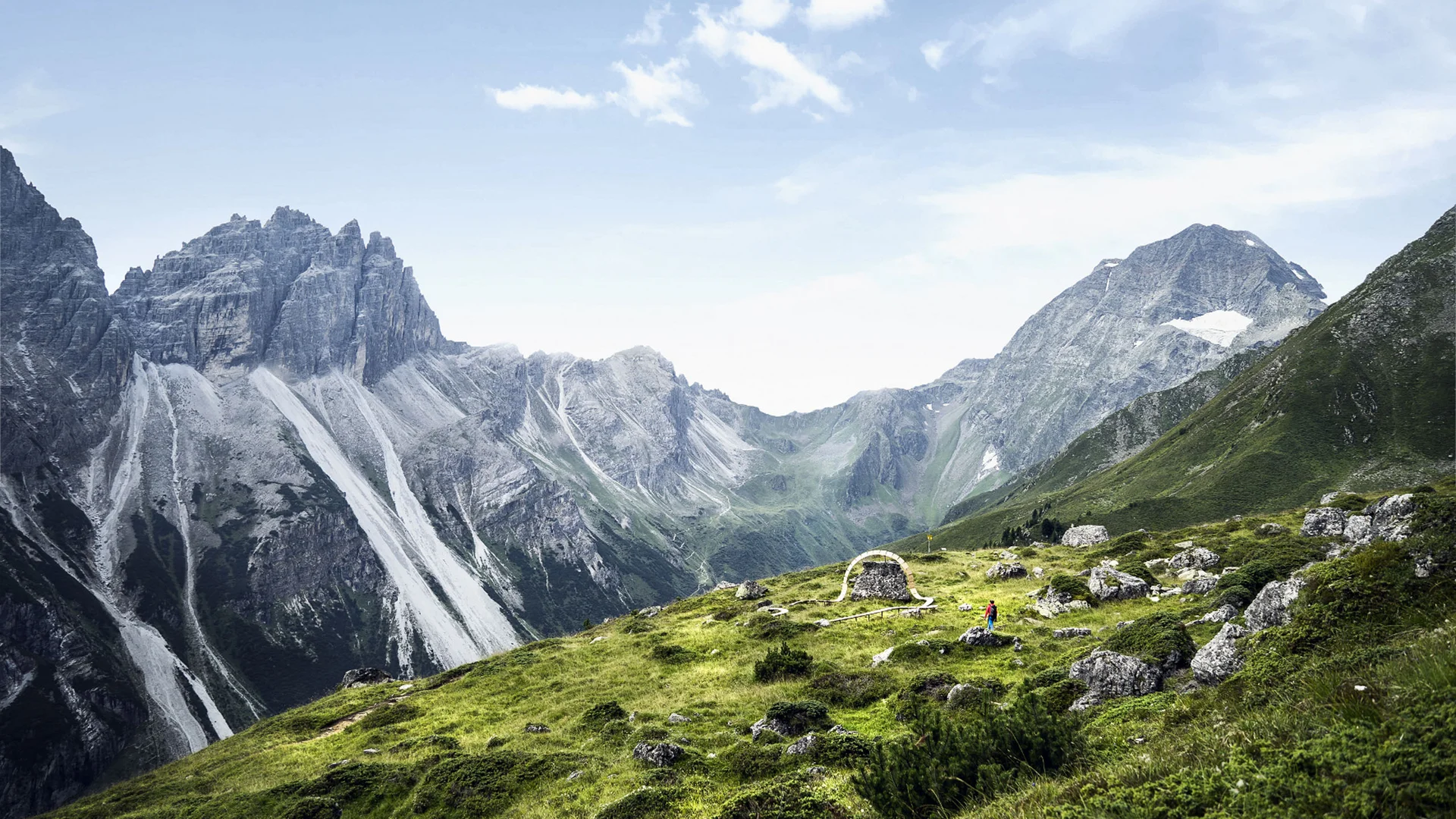 Mountain panorama with rugged peaks, green meadows and a hiker