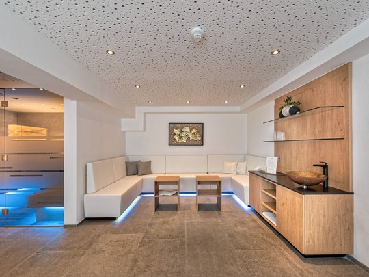 Ein feines Wellnesshotel in Fulpmes Moderner Wellness-Wartebereich mit weißem Sofa und Holzmöbeln neben einem blauen beleuchteten Raum