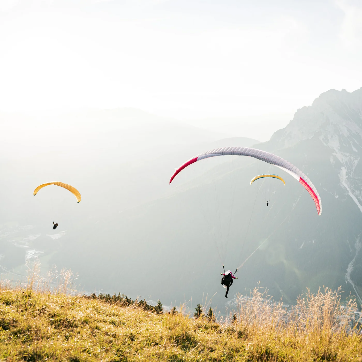 Several paragliders flying over a misty mountain landscape