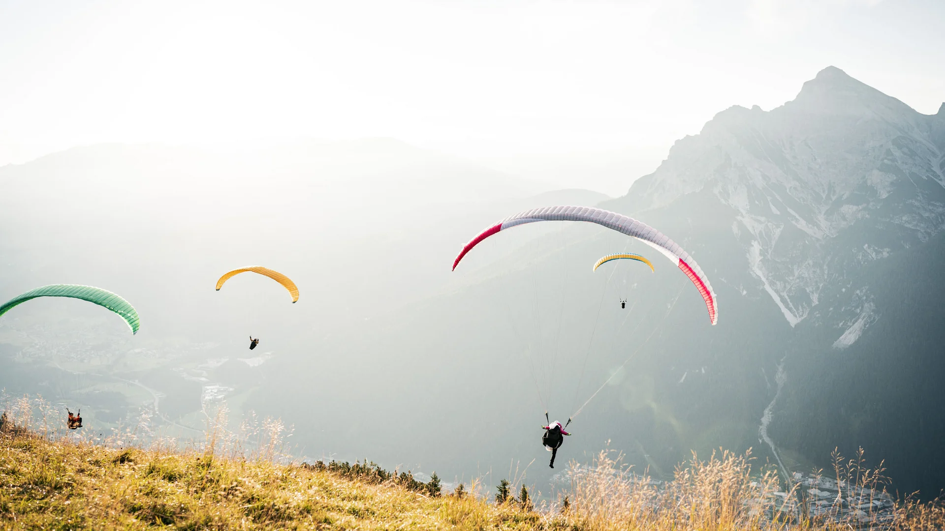 Several paragliders flying over a misty mountain landscape