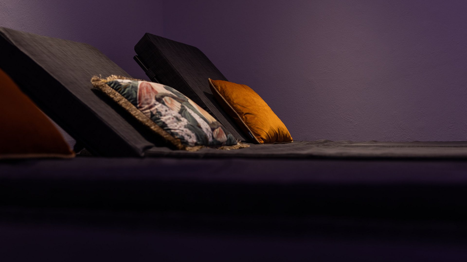 Unser Wellnesshotel im Stubaital Dunkle Relaxliegen mit bunten Kissen vor violetter Wand