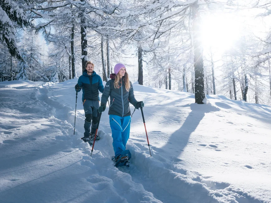 Two snowshoers walking through a snow-covered forest