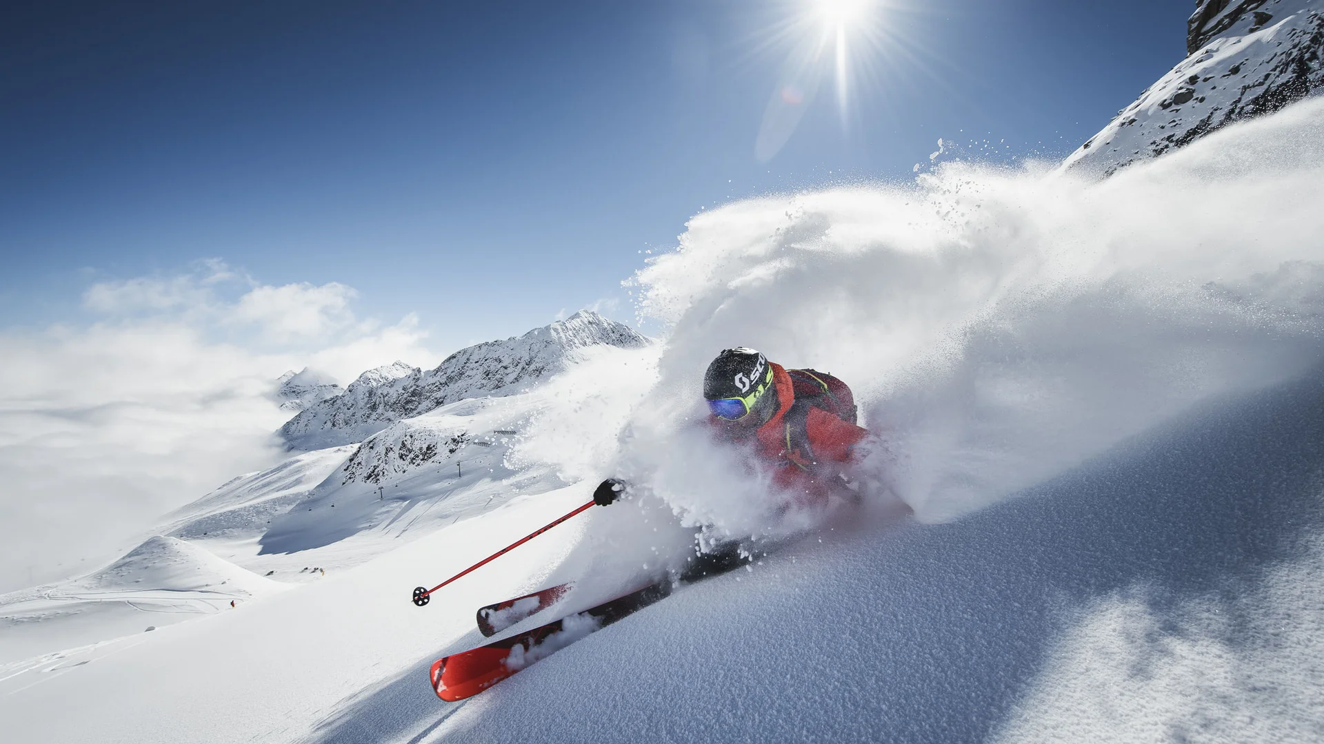 Skier carving through deep powder snow against a snowy mountain backdrop
