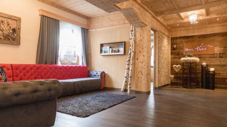 Einblicke in unser Hotel im Stubaital in Fulpmes Gemütliche Hotellobby mit rotem Sofa und Holzvertäfelung im Hotel Alphof