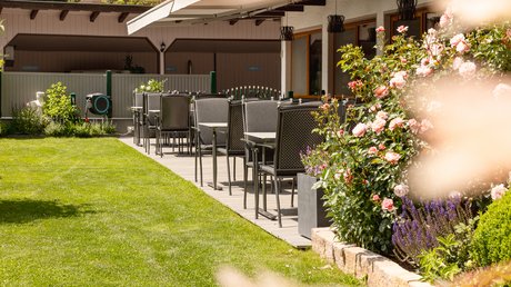 Einblicke in unser Hotel im Stubaital in Fulpmes Terrassenbestuhlung neben blühendem Rosenstrauch und gepflegtem Rasen