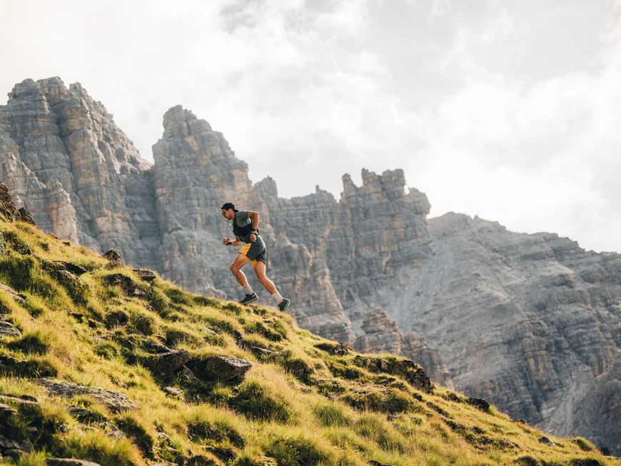 Runner on a grassy mountain slope with rugged rocky peaks in the background