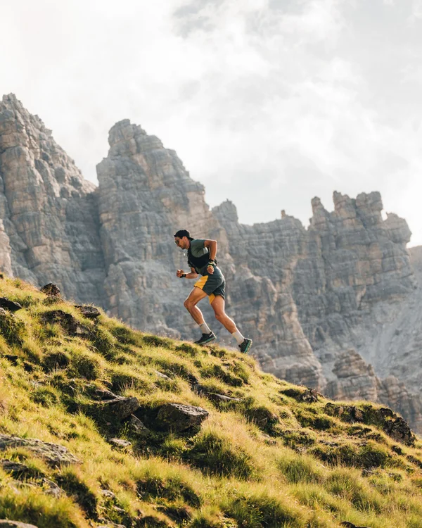 Runner on a grassy mountain slope with rugged rocky peaks in the background