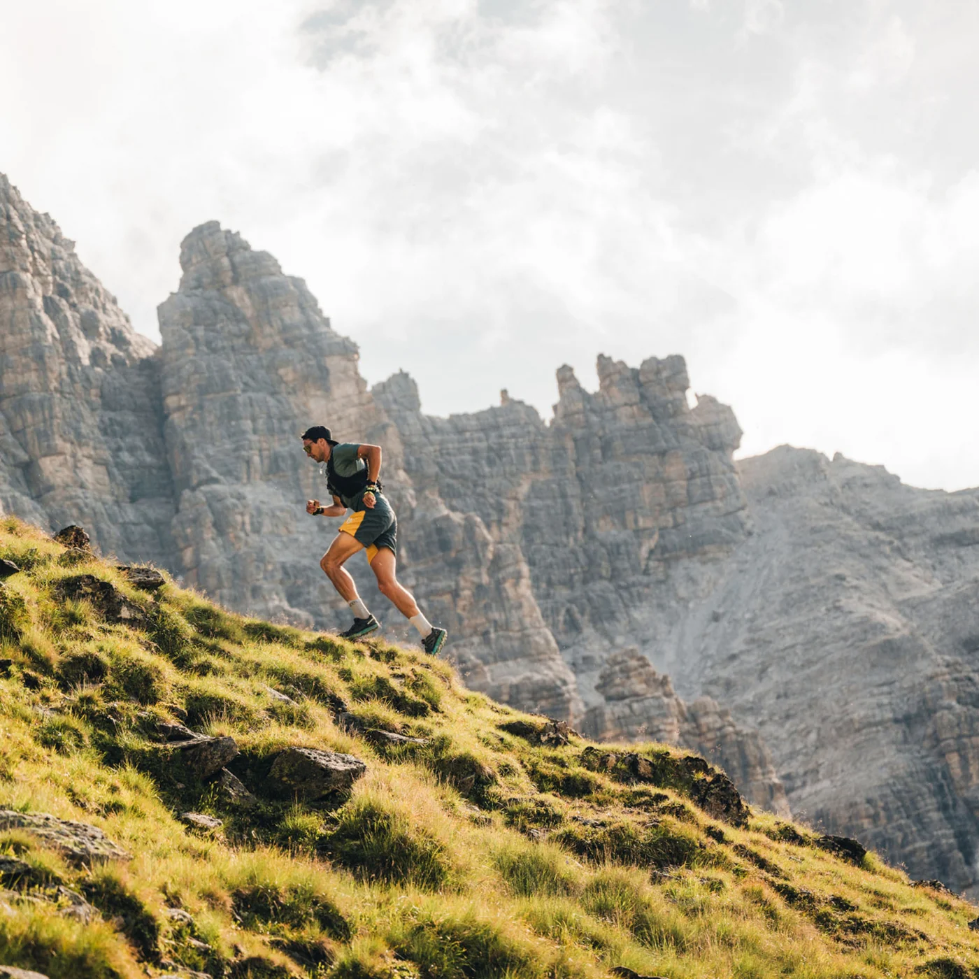 Runner on a grassy mountain slope with rugged rocky peaks in the background