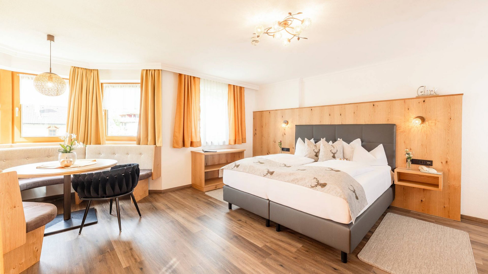 4-Sterne-Hotel Stubaital: Ihr Alphof erwartet Sie! Helles Hotelzimmer mit Doppelbett, Holzakzentwand und Sitzbereich am Fenster