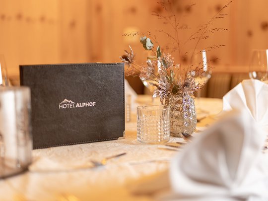 Ein feines Wellnesshotel in Fulpmes Eleganter gedeckter Tisch mit Hotel Alphof Speisekarte und Blumendekoration