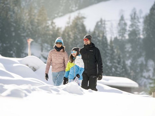 Winterurlaub in Tirol: Hotel Alphof in Fulpmes Familie mit Winterkleidung wandert im verschneiten Bergwald