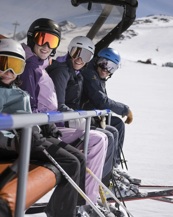 Four skiers seated on a chairlift above a snowy mountain landscape