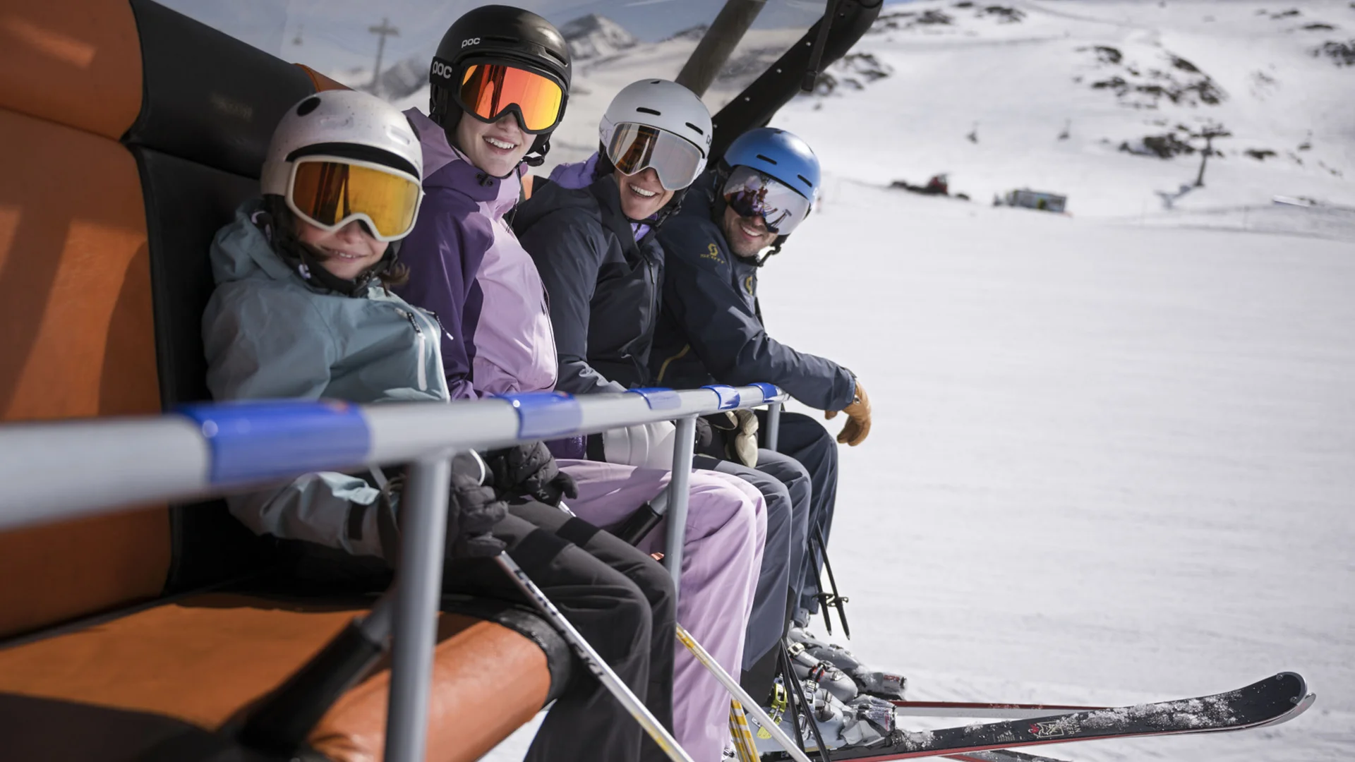 Four skiers seated on a chairlift above a snowy mountain landscape