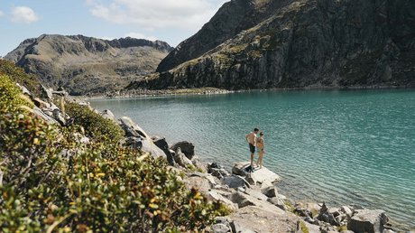Einblicke in unser Hotel im Stubaital in Fulpmes Zwei Personen am felsigen Ufer eines klaren Bergsees mit Bergen im Hintergrund