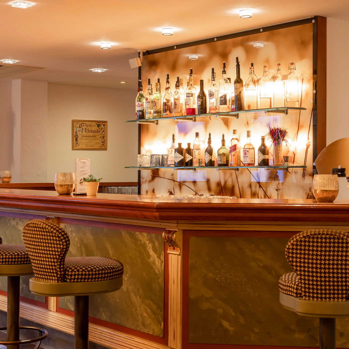 Alphof | genuine indulgence at a gourmet hotel in Tyrol Elegant hotel bar with stools and illuminated shelves displaying spirits