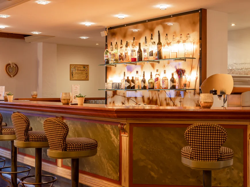 Alphof | genuine indulgence at a gourmet hotel in Tyrol Elegant hotel bar with stools and illuminated shelves displaying spirits