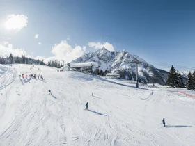 Skiers on a snowy slope with a cable car and snow-covered mountains