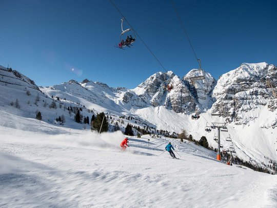 Winterurlaub in Tirol: Hotel Alphof in Fulpmes Skifahrer auf verschneiter Piste mit Sessellift und Bergen bei klarem Himmel