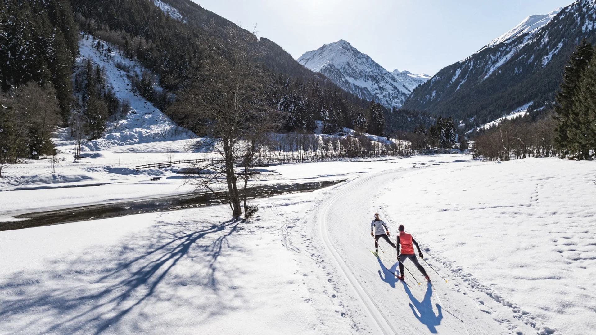 Two cross-country skiers on a snowy trail in a winter mountain landscape