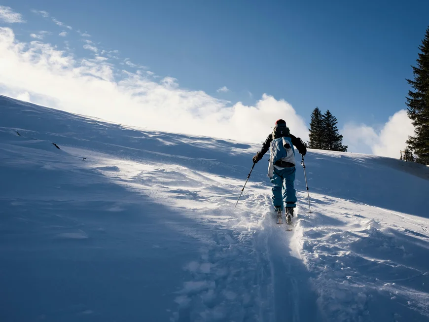 Skier climbing a snowy slope with poles