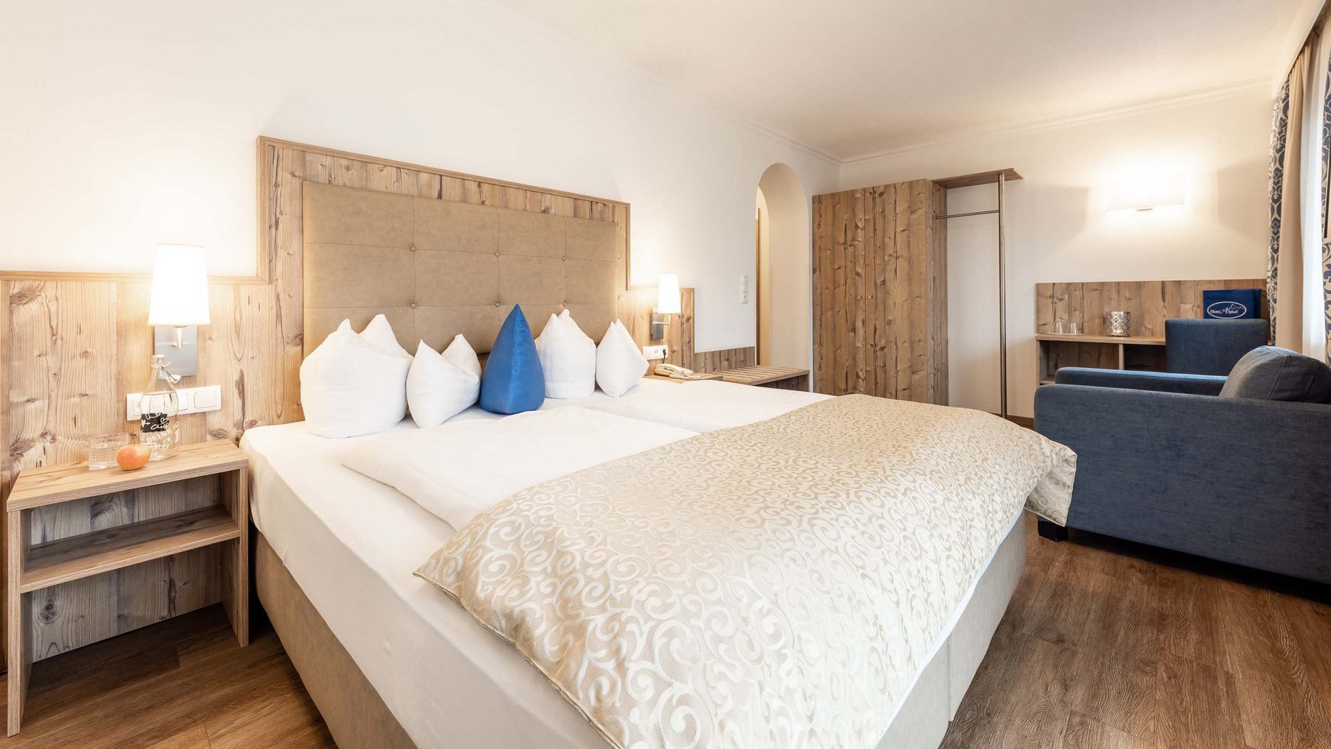 4-Sterne-Hotel Stubaital: Ihr Alphof erwartet Sie! Helles Hotelzimmer mit Doppelbett, Holzakzenten und Sitzbereich