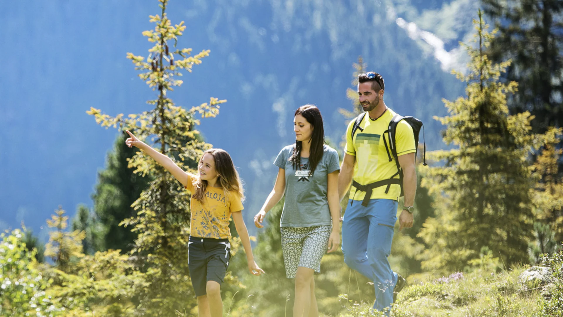 Family hiking through an alpine landscape with fir trees and mountain backdrop