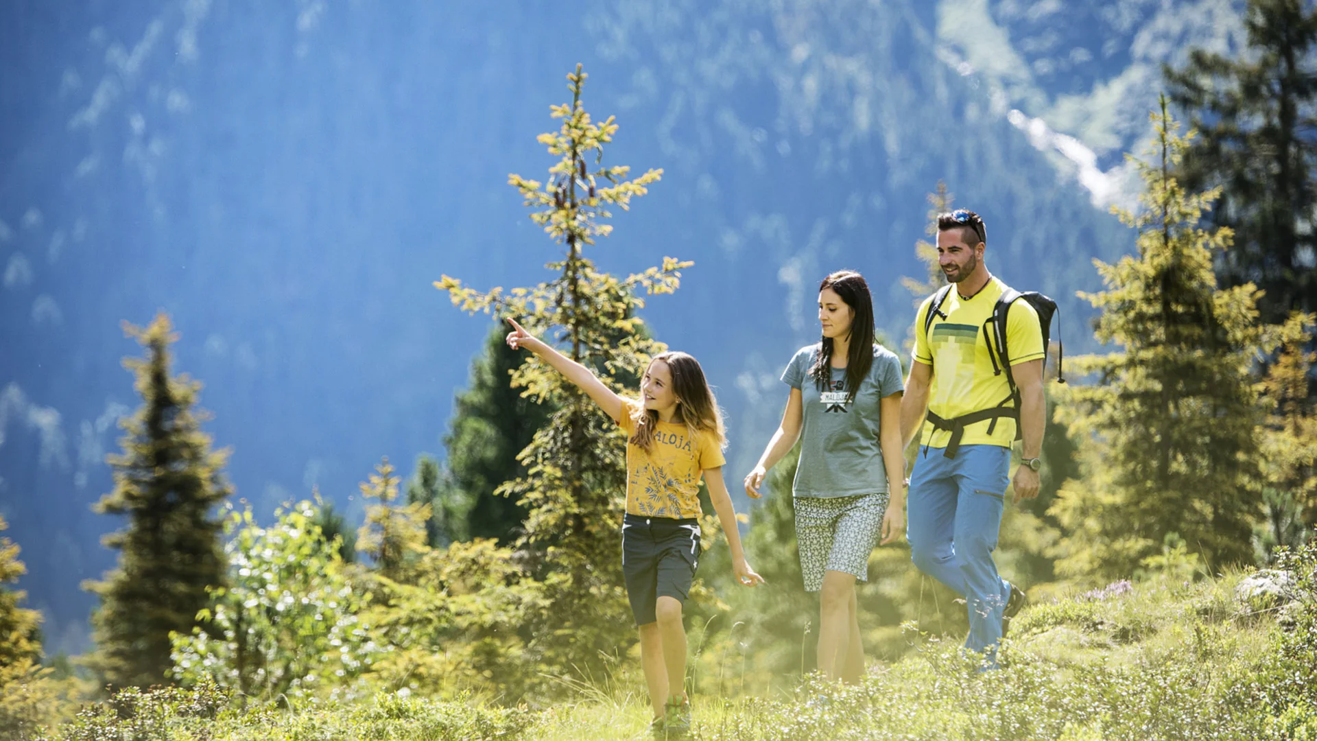 Family hiking through an alpine landscape with fir trees and mountain backdrop