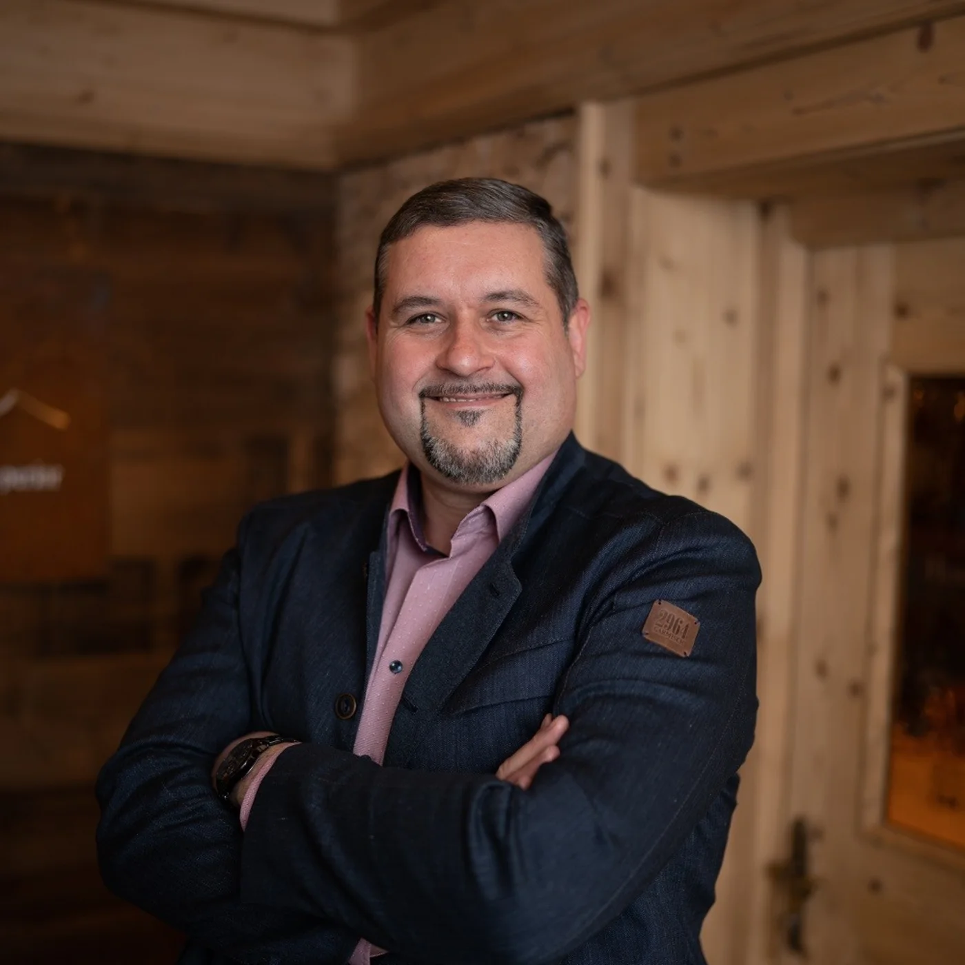 Portrait of a smiling man in a dark suit inside a rustic wooden cabin